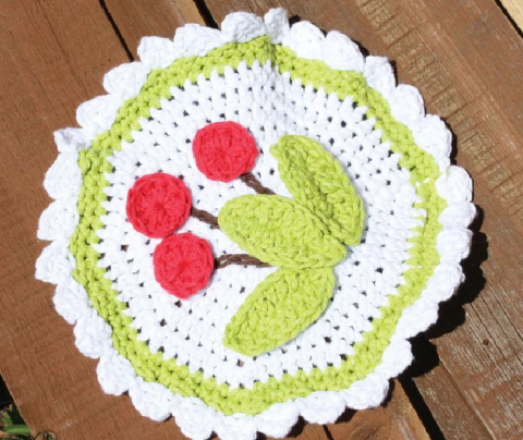 Round crochet dishcloth in white with red cherries. 