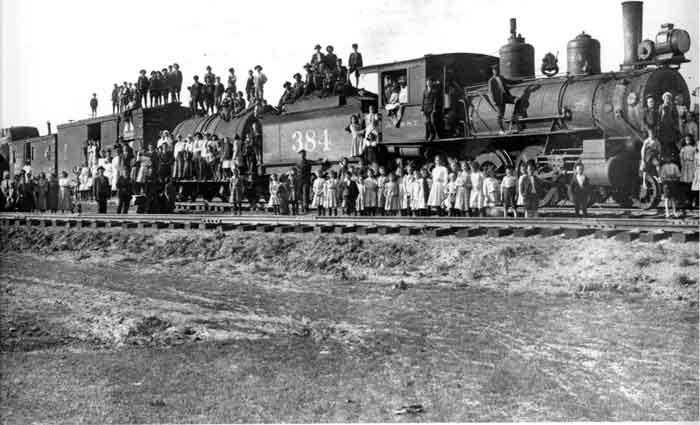 Old steam locomotive with small children standing in front of it.